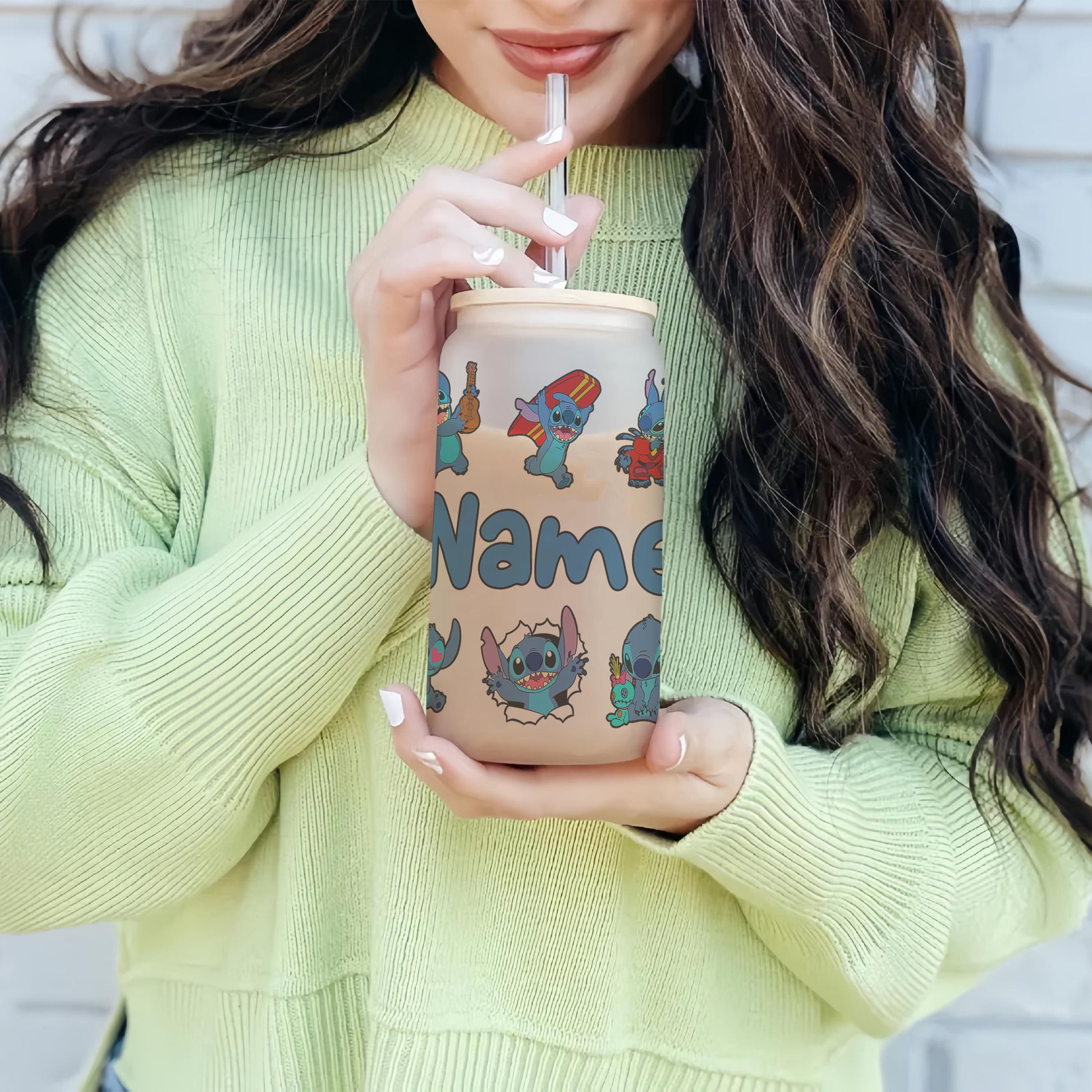 Person holding a tumbler with cartoon character design and 'Name' text, wearing a light green sweater.